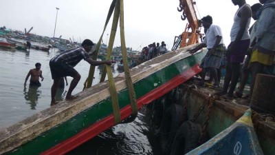 கிரேன் கொண்டு படகை தூக்கும் தொழிலாளிகள்