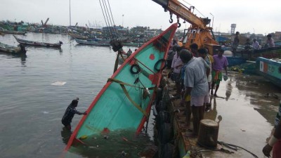 கிரேன் கொண்டு படகை தூக்கும் தொழிலாளிகள்