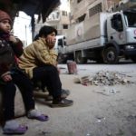 Children watch as an aid convoy of Syrian Arab Red Crescent drives through the besieged town of Douma