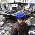 Syrian boy stands in front of damaged armoured vehicle belonging to Syrian army in a street in Homs